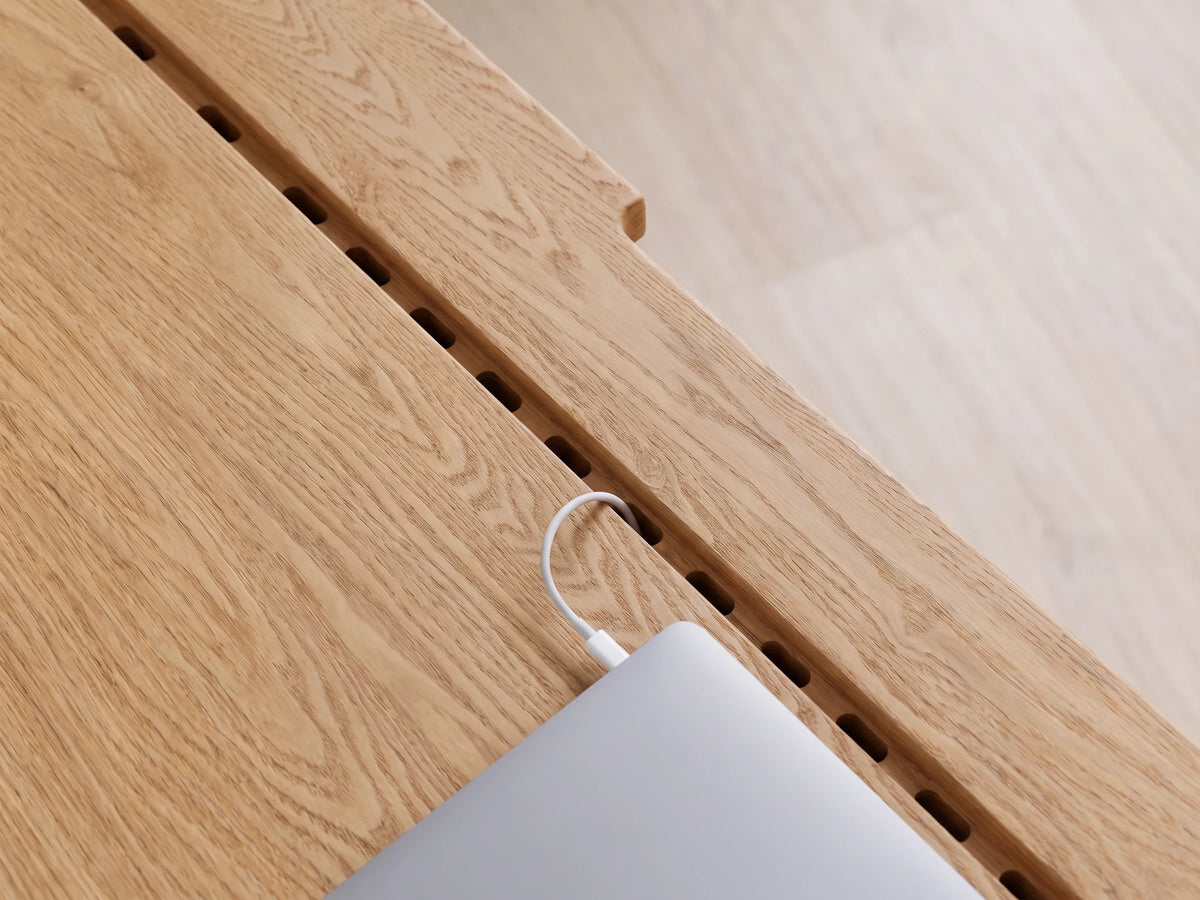 Masif meşe tablada oyulmuş kablo kanalı ve delikli tabanı, laptop şarj kablosu kanaldan geçiyor
